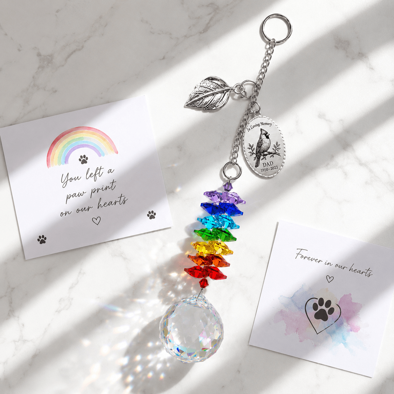 Hand holding personalized cardinal memorial crystal suncatcher outdoors with custom Dad oval charm, silver leaf charm, rainbow crystals, and sparkling crystal ball