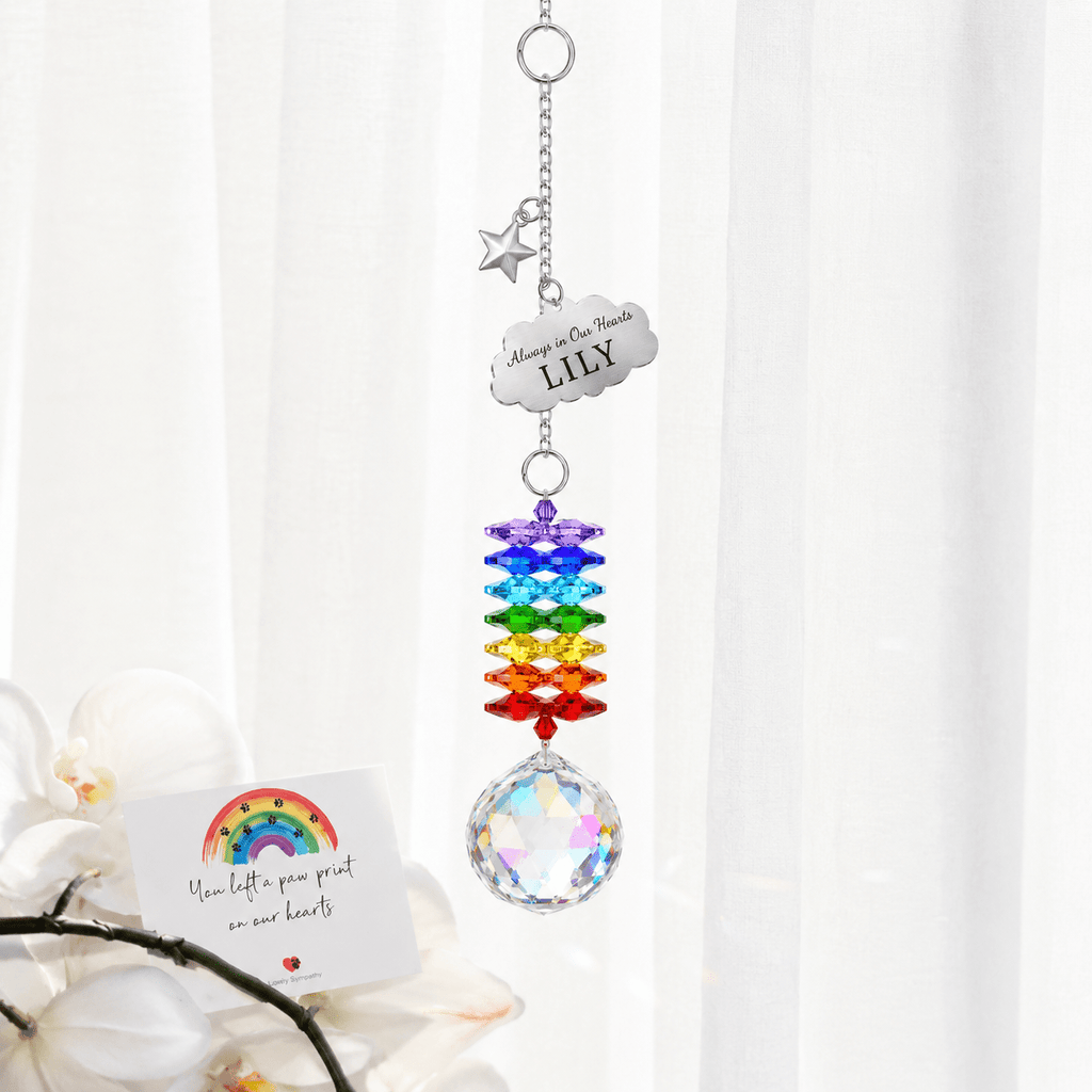 Personalized memorial cloud star crystal suncatcher hanging in front of sheer curtains with Rainbow Bridge sympathy card and soft floral decor
