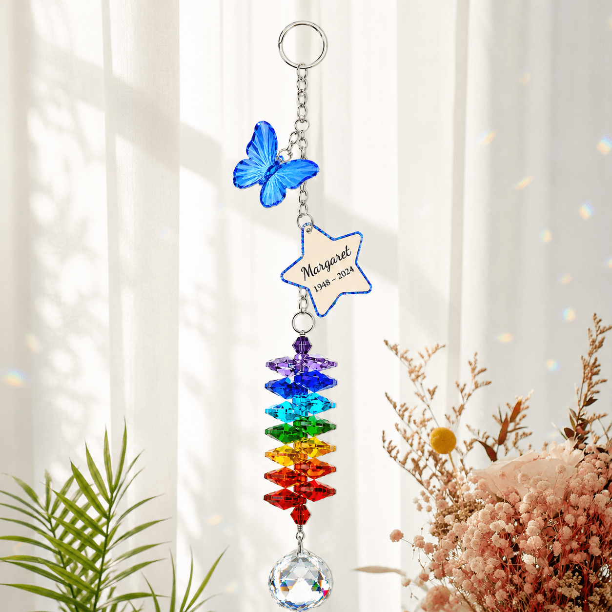 Personalized memorial butterfly crystal suncatcher hanging by a bright window with blue butterfly charm, custom star charm, rainbow crystals, and clear crystal ball