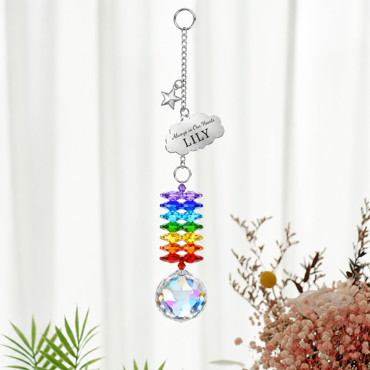 Personalized memorial cloud star crystal suncatcher hanging in front of soft white curtains with custom Lily cloud charm, silver star charm, rainbow crystals, and clear crystal ball