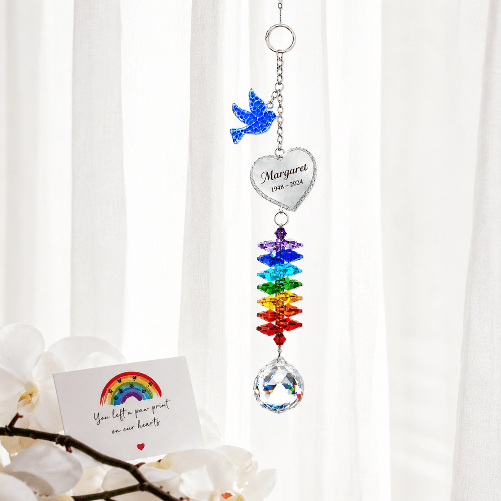 Personalized memorial dove crystal suncatcher hanging in front of sheer curtains with sympathy card and white orchid flowers