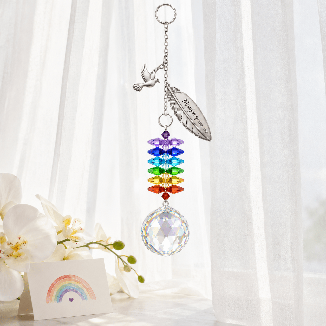 Personalized memorial feather dove crystal suncatcher hanging by a bright window with dove charm, custom feather charm, rainbow crystals, and clear crystal ball