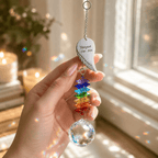 Hand holding personalized memorial angel wing crystal suncatcher near a sunny window with rainbow crystal reflections