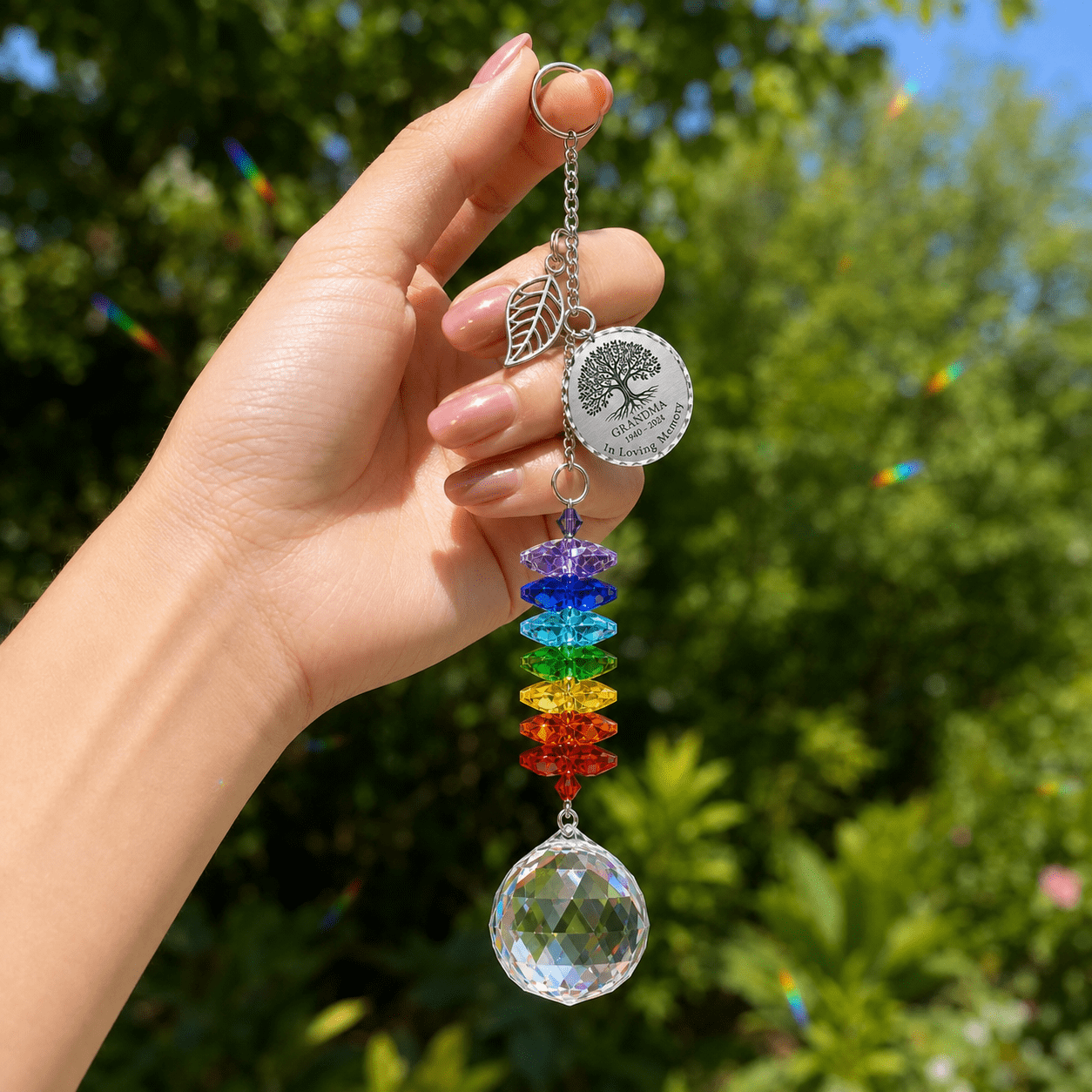Hand holding personalized Tree of Life memorial crystal suncatcher outdoors with custom Grandma round charm, leaf charm, rainbow crystals, and sparkling crystal ball