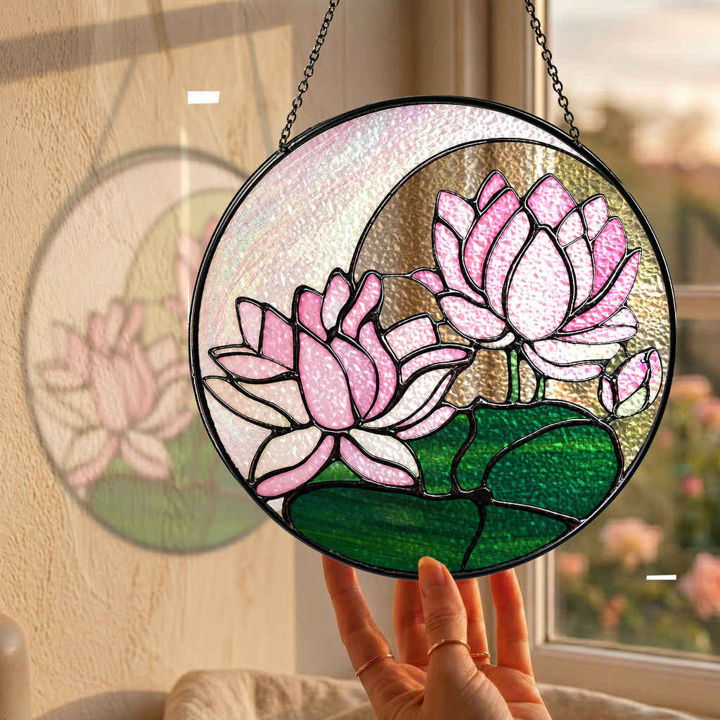 Pink lotus stained glass suncatcher hanging in a sunny window with a garden view