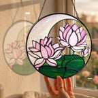 Pink lotus stained glass suncatcher hanging in a sunny window with a garden view