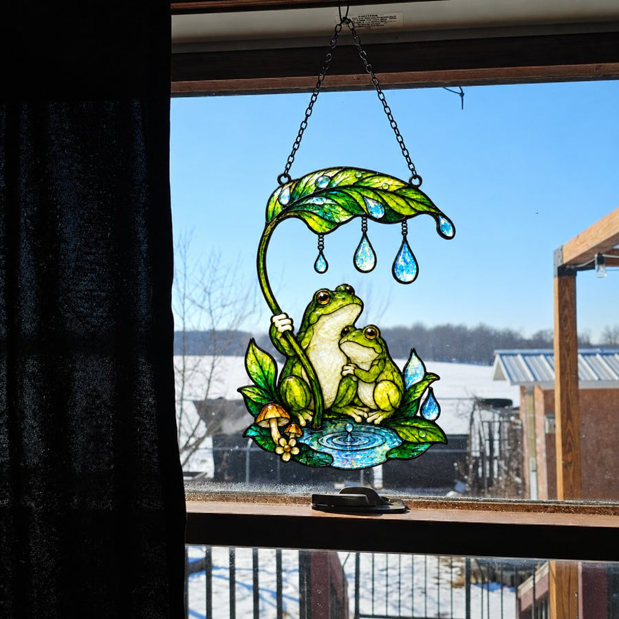 Frog Couple & Leaf Umbrella suncatcher in a window with dark curtain