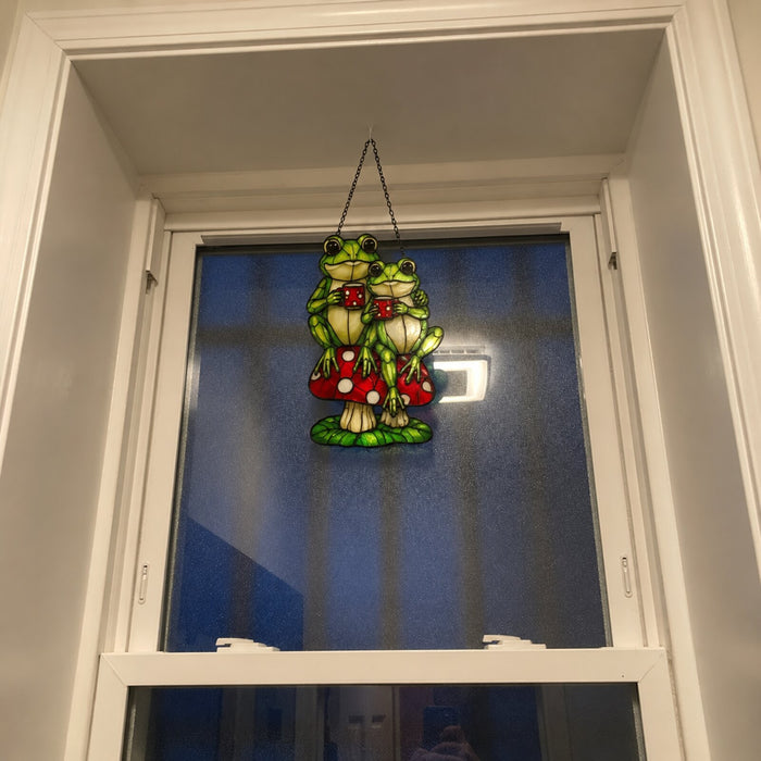 Frog Couple on Mushroom suncatcher in a tall white window at dusk
