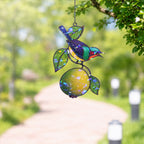 Stained glass style suncatcher with a colorful sunbird on a lemon branch, hanging in a sunlit window with rainbow light