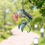 Stained glass style suncatcher with a hummingbird on a coral morning glory vine, hanging in a sunlit window with rainbow light