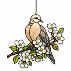 Stained glass style suncatcher with a mourning dove on a branch of white blossoms, hanging in a sunlit window with rainbow light