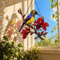 Stained glass style suncatcher with a colorful sunbird on a branch of red hibiscus flowers, hanging in a sunlit window with rainbow light