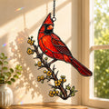 Stained glass style suncatcher with a red northern cardinal on a branch of golden berries, hanging in a sunlit window with rainbow light