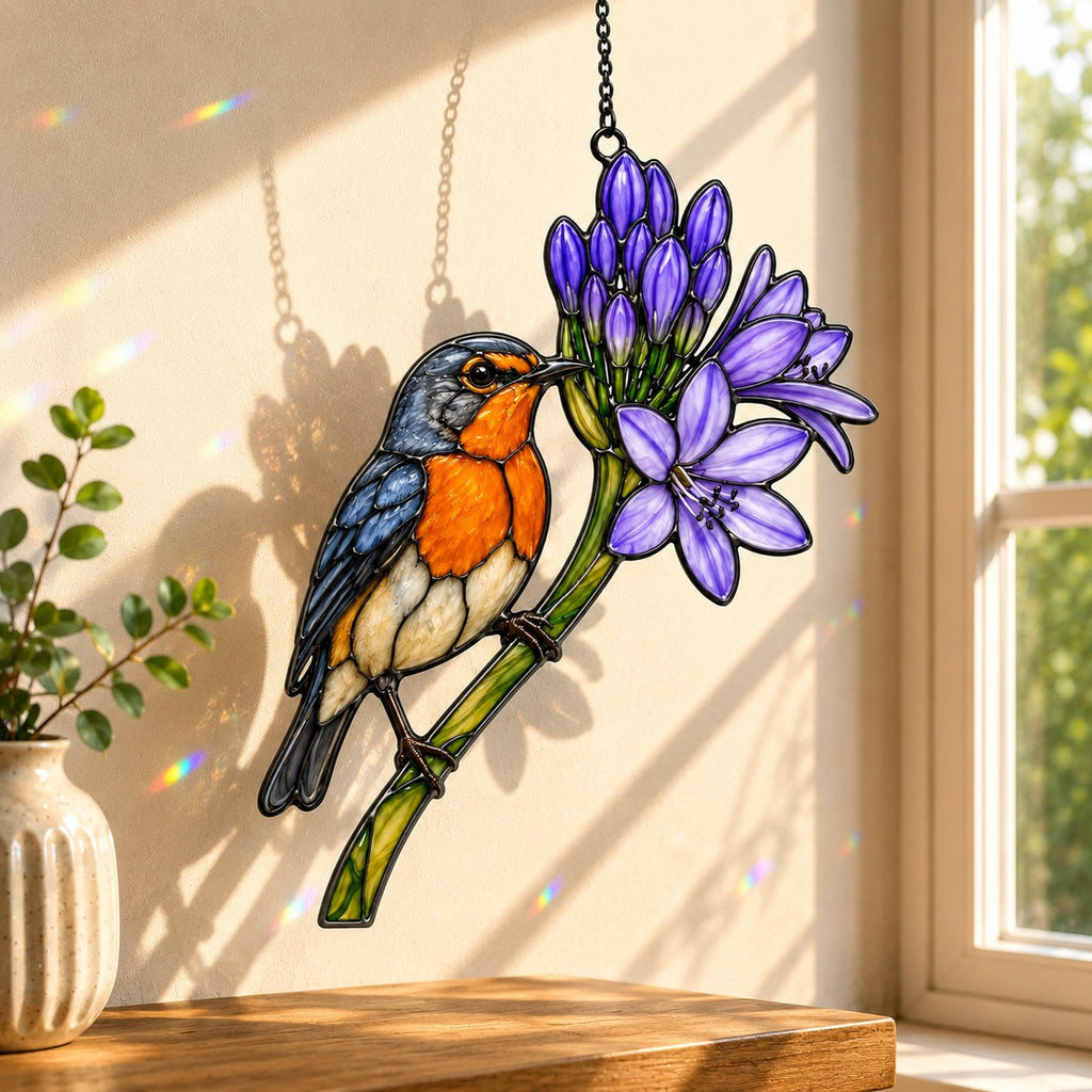 Stained glass style suncatcher with a bluebird beside purple agapanthus flowers, hanging in a sunlit window with rainbow light