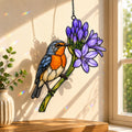 Stained glass style suncatcher with a bluebird beside purple agapanthus flowers, hanging in a sunlit window with rainbow light