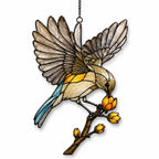 Stained glass style suncatcher with a songbird with open wings on a branch of golden buds, hanging in a sunlit window with rainbow light