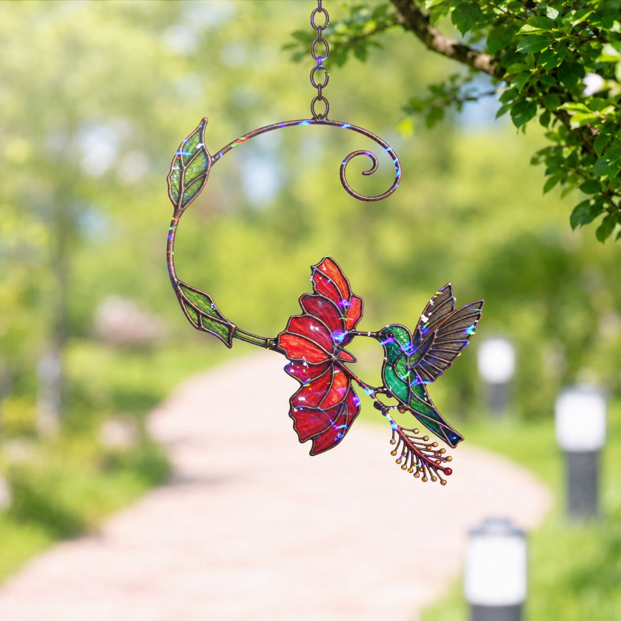 Stained glass style suncatcher with a hummingbird at a red bloom on a curling vine, hanging in a sunlit window with rainbow light