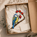 Stained glass style suncatcher with a blue tit on a branch of red rosehips, hanging in a sunlit window with rainbow light