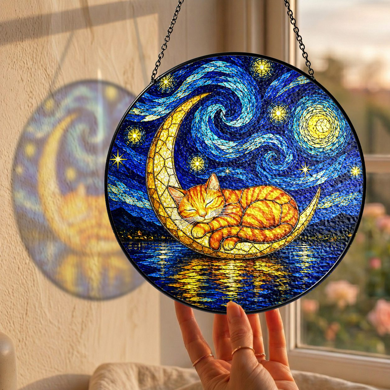 Hand holding the cat moon suncatcher at a window