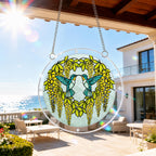 Round hummingbird acrylic puzzle suncatcher hanging in natural sunlight beside a balcony window.