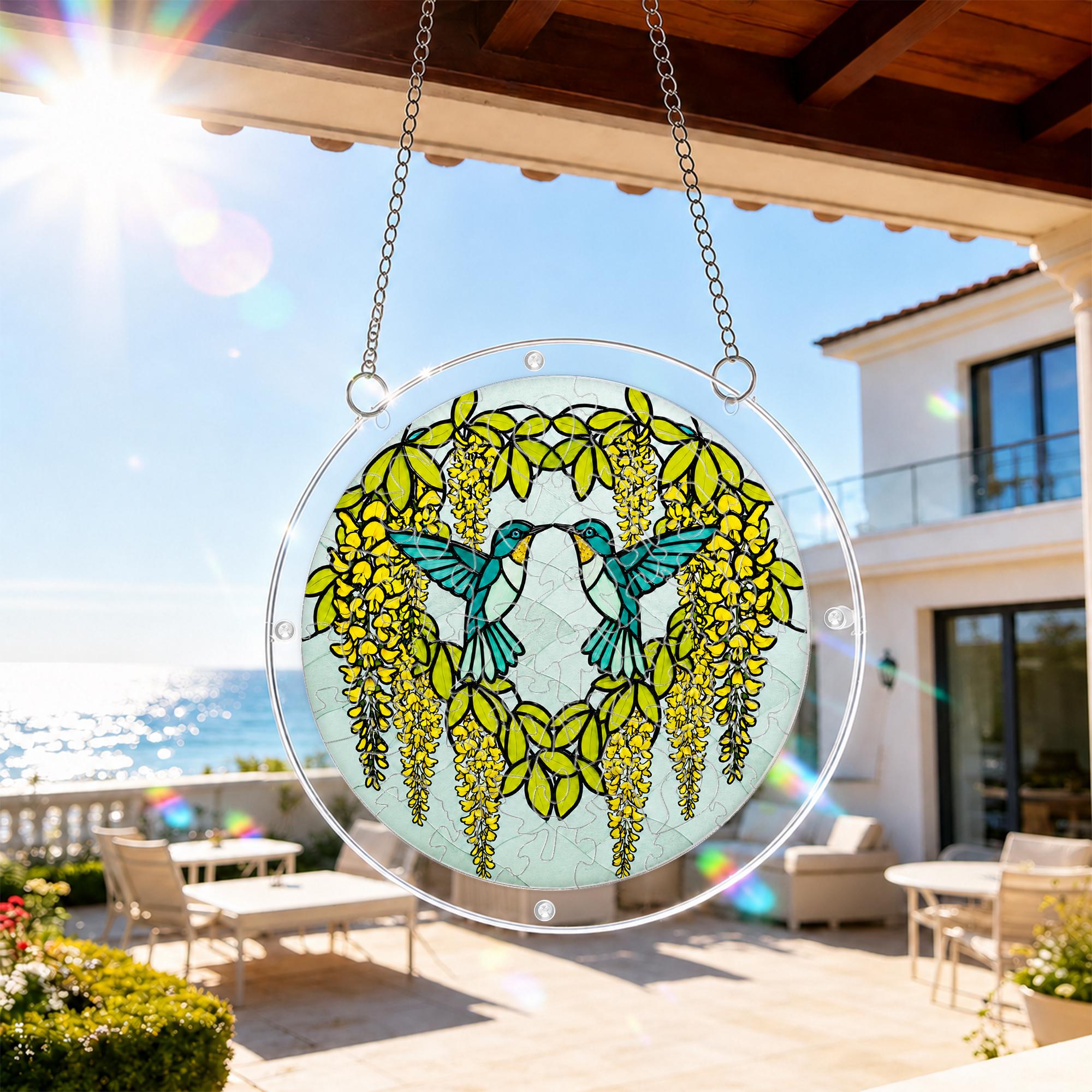 Round hummingbird acrylic puzzle suncatcher hanging in natural sunlight beside a balcony window.