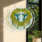 Round hummingbird puzzle suncatcher hanging in a sunlit window with yellow cascading flowers and green leaves.