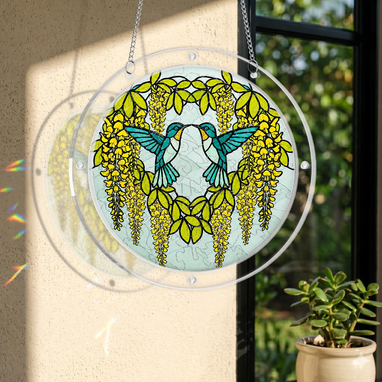 Round hummingbird puzzle suncatcher hanging in a sunlit window with yellow cascading flowers and green leaves.