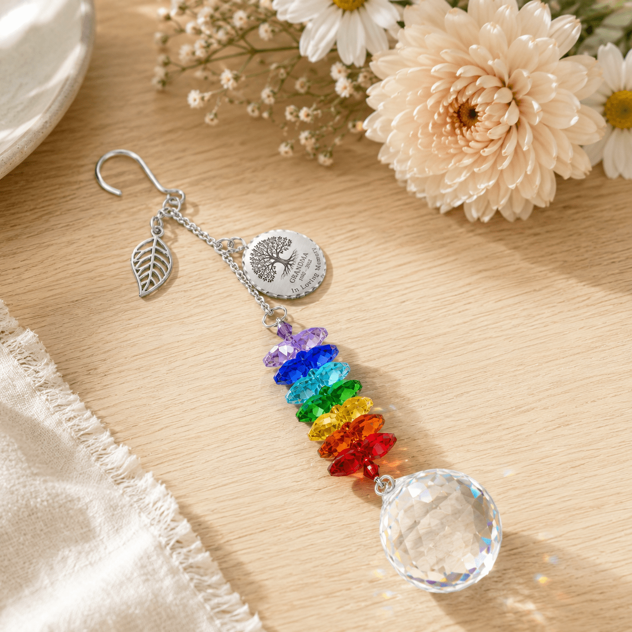 Personalized Tree of Life memorial crystal suncatcher displayed on wooden tabletop with leaf charm, custom Grandma round charm, rainbow crystals, and crystal ball