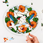 Hand assembling a two hummingbirds orange flower acrylic puzzle suncatcher with colorful puzzle pieces