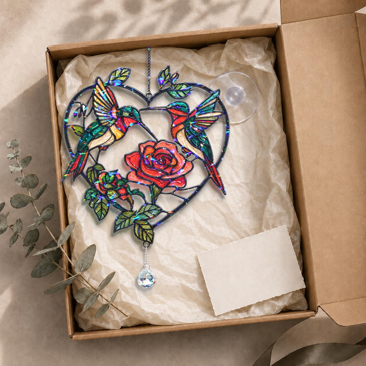 Two hummingbirds rose heart holographic acrylic suncatcher displayed in a kraft gift box with tissue paper and adhesive hook.
