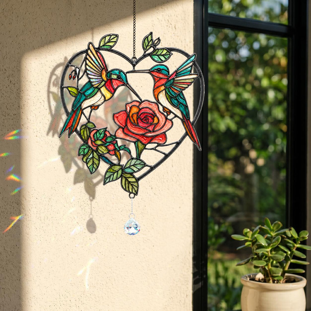 Two hummingbirds rose heart holographic acrylic suncatcher hanging by a sunny window with rainbow reflections and plant decor.